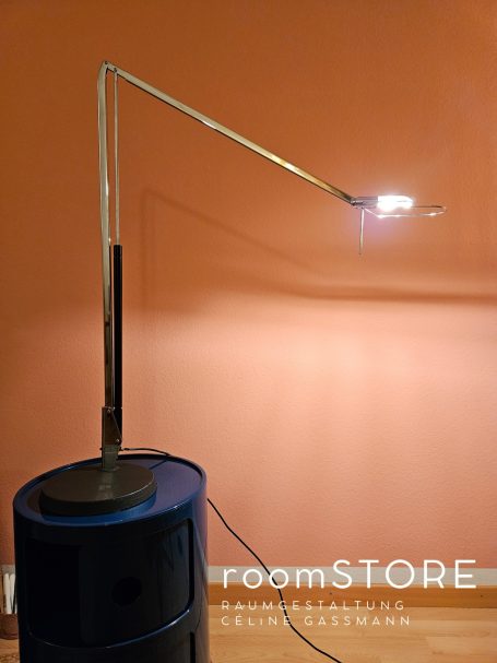 Belux Lifto Lampe 310.- Stehlampe mit schwenkbarem Arm und runder Basis vor einer orangefarbenen Wand.