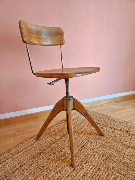 Girsberger Stuhl Hölzerner Stuhl mit drehbarem Sitz und Holzrückenlehne vor rosa Wand.