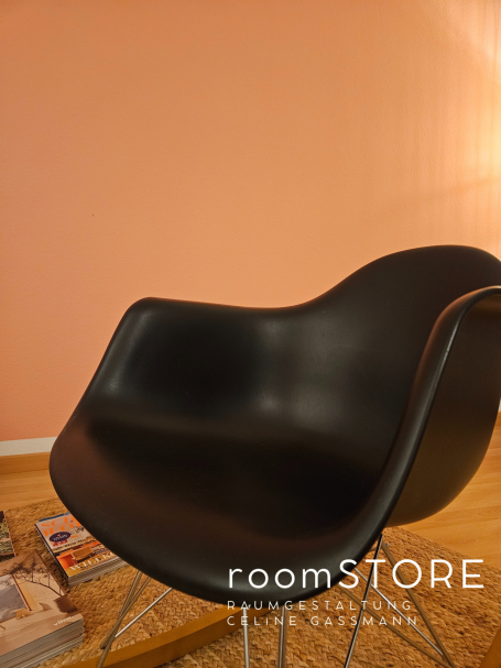 Vitra Rocking Armchair Rod Base 420.- Schwarzer Stuhl vor einer hellrosa Wand, daneben liegen einige Zeitschriften.