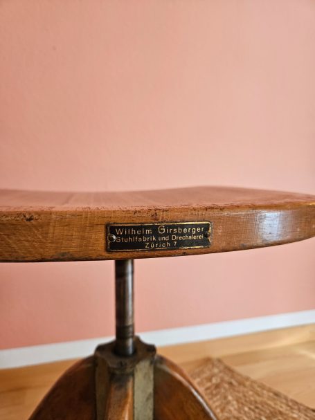 Girsberger Stuhl Holztisch mit Metallgestell, braune Oberfläche, vor rosa Wand.